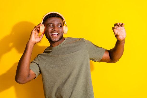 照片上积极乐观的男人，女人，穿着卡其色的衣服，听音乐，看起来空旷的空间孤立在黄色的背景图片下载