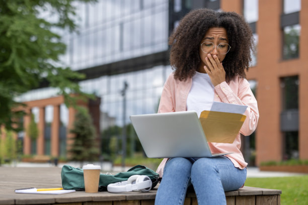 忧心忡忡的女学生在校校外边看信边用笔记本电脑图片下载