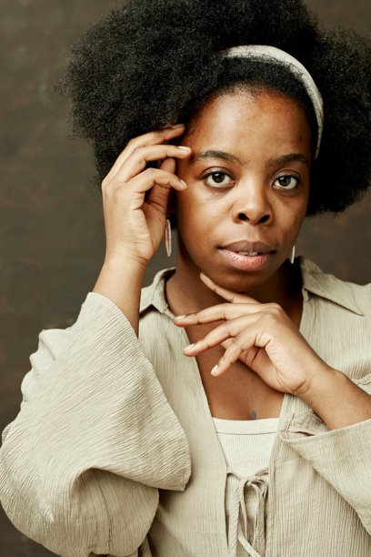 黑人妇女在棕色背景上看镜头触摸脸的肖像图片下载