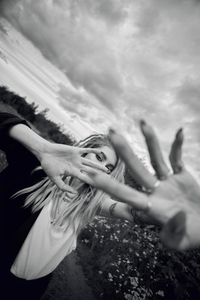 一个留着脏辫的女人在田野里用手捂着脸摆姿势。这张照片是黑白的，天空多云图片下载