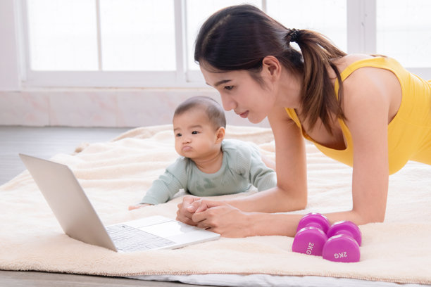 亚洲妈妈产后锻炼，年轻妈妈用笔记本电脑看视频训练减肥瑜伽运动，美女和蹒跚学步的婴儿一起玩耍，充满爱和关怀图片下载