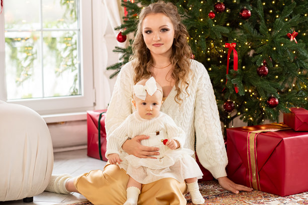 美丽的黑发母亲和小女儿坐在客厅的地板上，旁边是一棵美丽的圣诞树图片下载