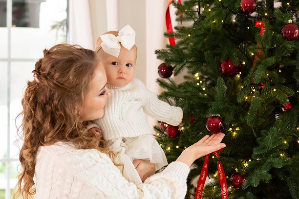 一位美丽的母亲向她的小女儿展示一棵优雅的圣诞树的特写。母亲抱着一个孩子，背景是一棵为圣诞节和新年装饰的圣诞树。幸福家庭理念图片下载