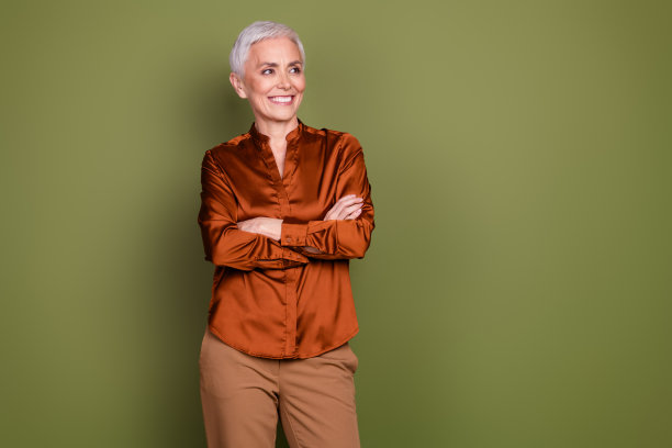 照片中，漂亮的退休女性双手交叉，看起来空无一人，穿着时髦的棕色正装，衬托着卡其色的背景图片下载
