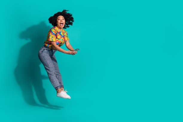 全身照片兴奋积极的女人穿印花t恤跳高短信设备空白空间孤立蓝绿色背景图片下载