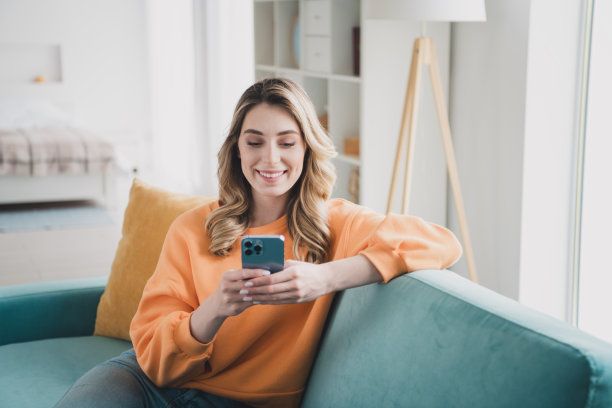 漂亮女孩的照片肖像坐在沙发上拿着装置穿着橙色的衣服现代室内平坦的室内图片下载