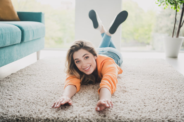 年轻女子躺在地板上的全尺寸照片，梦幻般的放松伸展穿着橙色的衣服舒适的日光家室内客厅图片下载