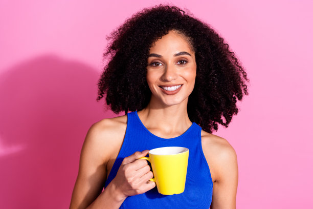 照片中微笑的女孩端着咖啡杯，穿着休闲的衣服孤立的粉红色背景图片下载