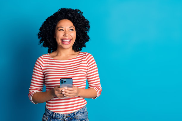 照片正面迷人的女孩穿着时髦的衣服，抱着现代的小玩意，在蓝色的背景上孤立的空间图片下载