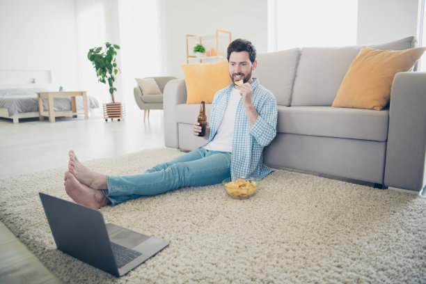 成年男子呆在家里的照片在他的新房子在室内客厅坐在地板上吃薯条喝啤酒看足球比赛图片下载