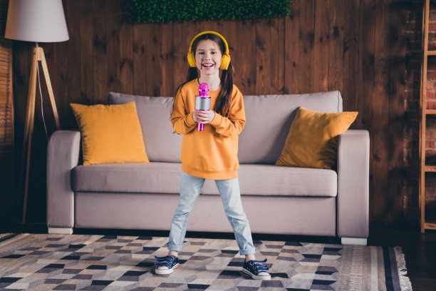 迷人的小女孩的全身照片耳机麦克风唱卡拉ok穿着橙色的衣服花休闲宽敞的房子在室内房间图片下载