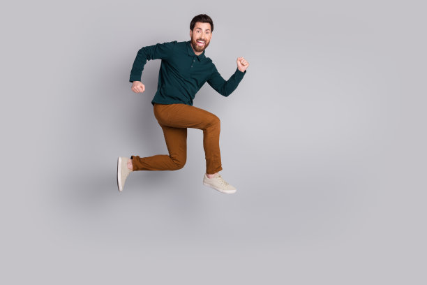 照片中，疯狂有趣的积极向上的男人穿着时髦的绿色衣服跑得飞快，空白的空间孤立在灰色的背景上图片下载