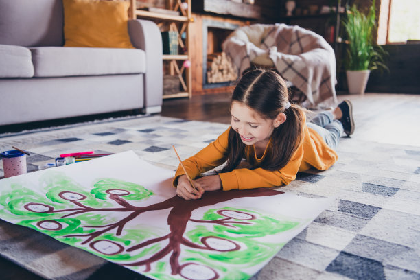 迷人的小女孩躺在地板上画家谱的全身照片，穿着橙色的衣服在宽敞的房间里消磨时光图片下载