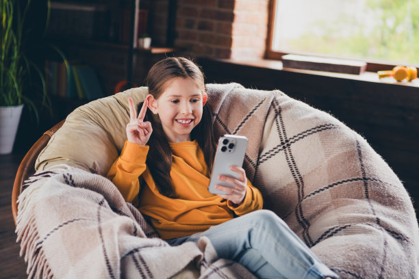 照片中，漂亮开朗的小女孩穿着黄色套头衫，脸上挂着v字，在房间里自拍现代小工具图片下载