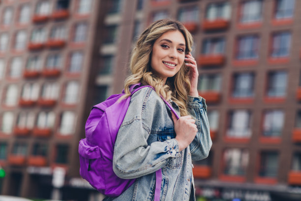 漂亮的年轻女子的资料照片携带背包触摸头发穿着牛仔夹克走在城市中心户外图片下载