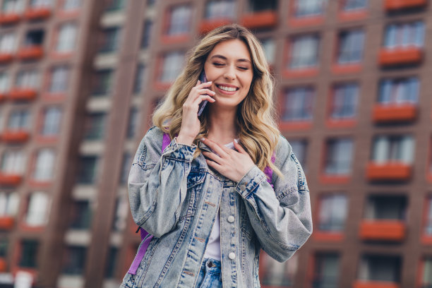 漂亮的年轻女子的照片讲电话笑背包穿牛仔夹克走市中心户外图片下载