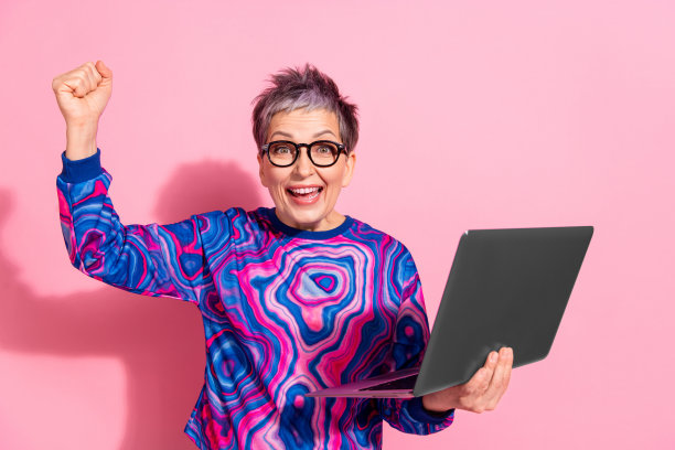 照片肖像迷人的高级妇女赢得上网本穿着蓝色的彩色衣服孤立在粉红色的背景图片下载