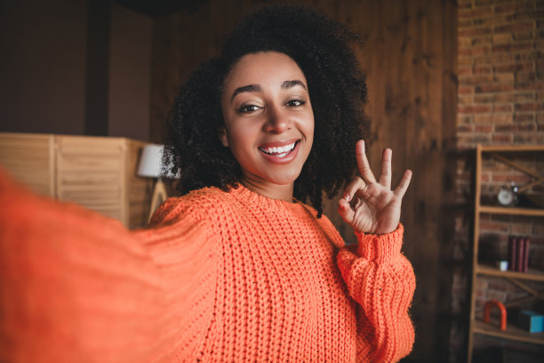 积极的好心情的女人穿着橙色套头衫的照片，自拍显示了放松的家在室内的房子公寓房间图片下载