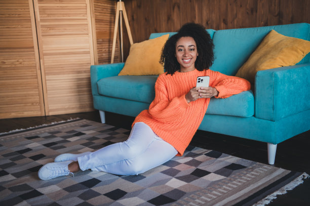 照片的闪亮可爱的女孩穿着橙色套头衫呆在家里打字短信现代设备在室内的房子公寓房间图片下载