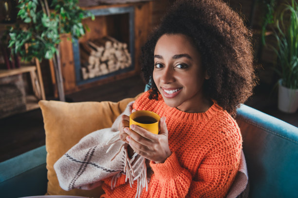 闪亮可爱的女孩穿着橙色套头衫的照片，在家里的房子公寓房间里喝茶图片下载