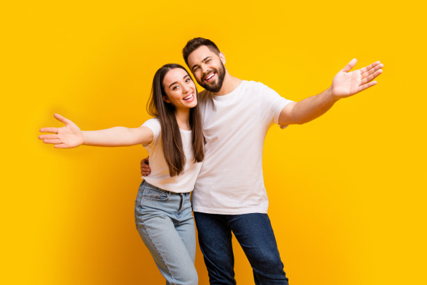 照片肖像迷人的年轻男子，女子拥抱伸展双手欢迎穿着时尚的白色衣服孤立在黄色的背景图片下载
