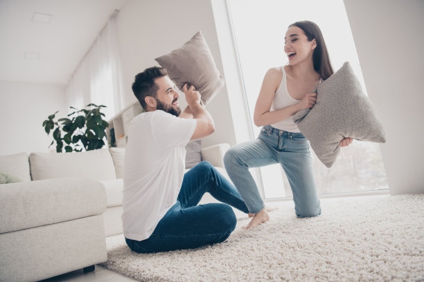 漂亮的开朗的女士的照片，男人穿着休闲的样子，微笑着在房间里享受枕头大战图片下载