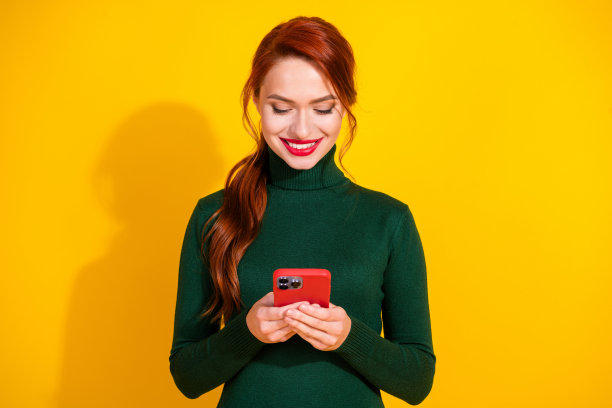 照片中闪亮迷人的女士穿着绿色毛衣发短信，苹果，iphone，三星设备空白空间孤立的黄色背景图片下载