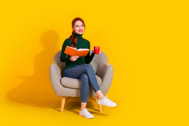 全身照片闪亮迷人的女士穿着绿色毛衣，放松的椅子，享受故事，喝茶，空旷的空间，孤立的黄色背景图片下载