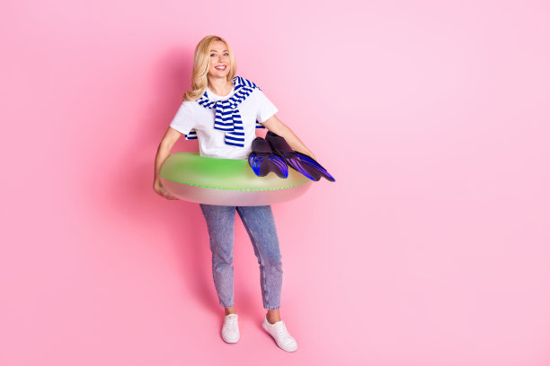 漂亮的年轻女性充气环形脚蹼的全尺寸照片，穿着时髦的白色衣服，孤立在粉红色的背景上图片下载