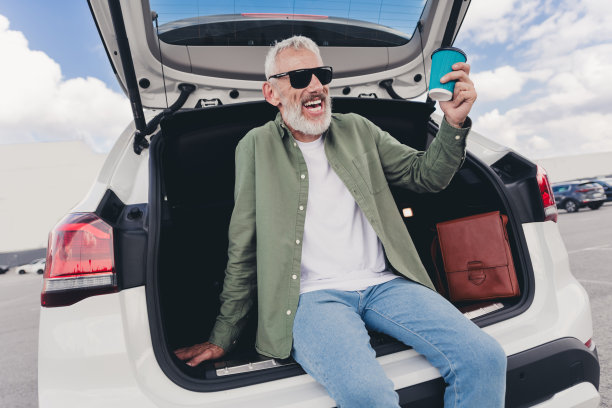 迷人有趣的退休男子穿着卡其布衬衫坐在汽车后备箱享受咖啡到户外城市街道的照片图片下载