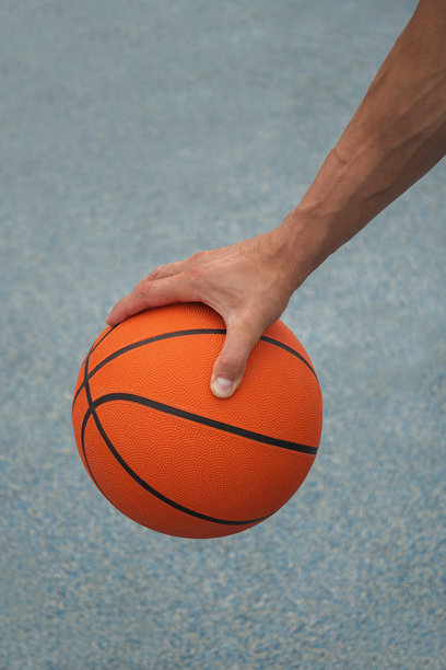 在蓝色的球场上，男子手里拿着橙色的篮球。运动背景。图片下载