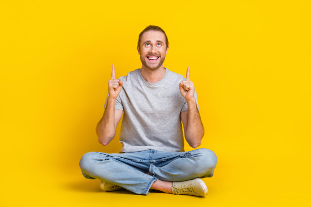 搞笑男人的全尺寸照片，灰色t恤裤子坐在地板上，看起来在黄色背景上孤立的提供空白空间图片下载