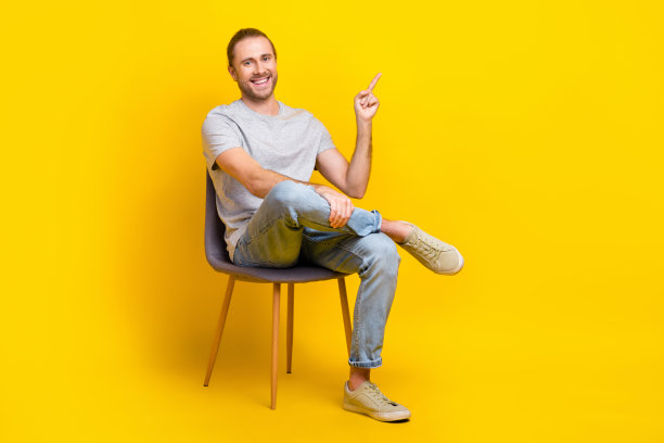 快乐的男人的全尺寸照片灰色t恤裤子坐在椅子上指导销售空白空间孤立的黄色背景图片下载