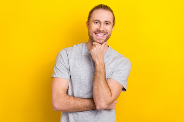 乐观积极的成功男人的照片，穿着灰色的衣服，手臂摸脸，在黄色背景上解决问题图片下载