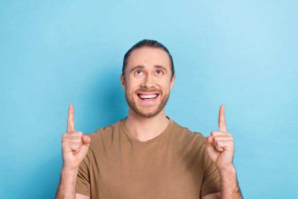 年轻的学生商人穿着棕色时髦的t恤的照片直接手指看模拟新的it专家空缺孤立在蓝色的背景图片下载