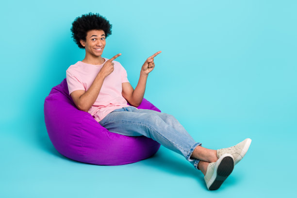 青年广告人穿休闲服的全身照片表明手指空白空间pouf推荐产品孤立的青色背景图片下载