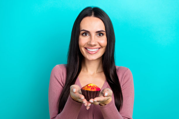 积极的年轻女厨师的特写照片拿着她的第一个手工新鲜出炉的松饼吃甜美味的甜点孤立的青色背景图片下载