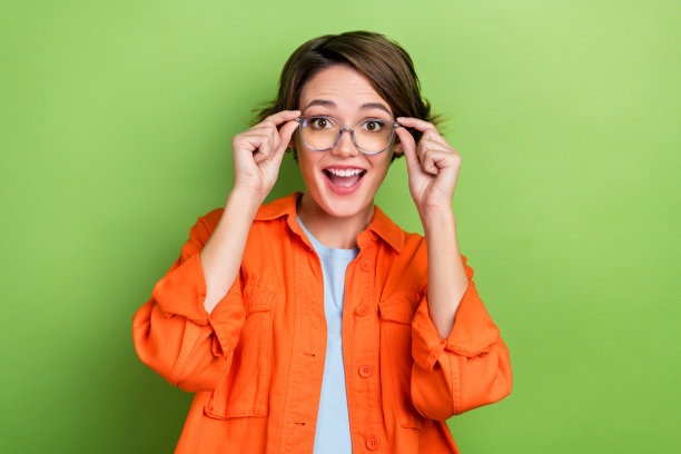 照片上的积极高兴可爱聪明的女士穿着时髦的橙色衣服，在绿色的背景上快乐地保持着优质的配饰图片下载