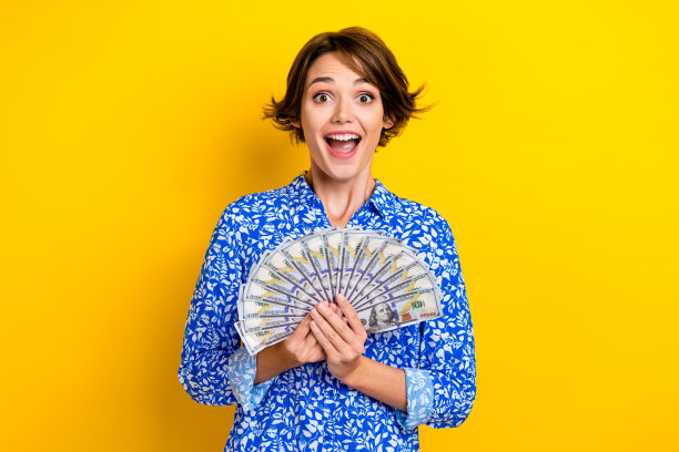照片开朗积极的女士拿着钱高兴赢得彩票头奖奢侈的生活孤立在黄色的背景图片下载