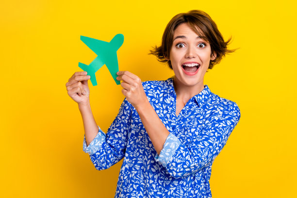 照片肖像可爱的年轻女士拿着纸飞机兴奋的旅行社穿着时髦的印花衣服孤立在黄色的背景图片下载
