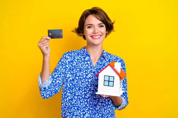 照片肖像可爱的年轻女士拿着小房子信用卡保险穿着时尚的印花看起来孤立的黄色背景图片下载