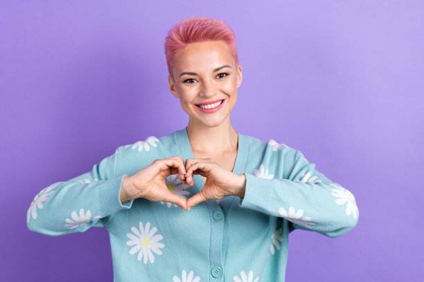 照片中乐观满意的女性短发，穿着蓝色开衫手臂，紫色背景上的心脏被孤立图片下载