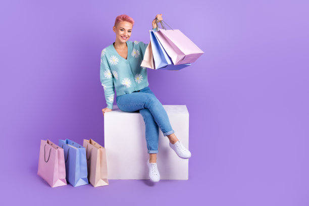 购物狂女人的全身照片时尚达人持有大量便宜货廉价衣服促销立方体消费主义孤立在紫色的背景图片下载