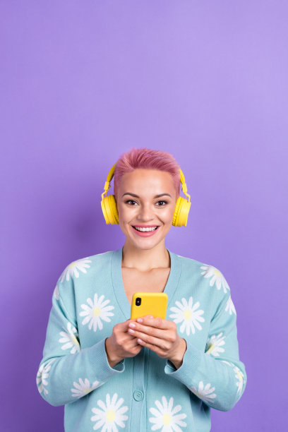 照片积极开朗的女人短发穿着蓝色开襟羊毛衫拿着电话听播放列表孤立的紫色背景图片下载