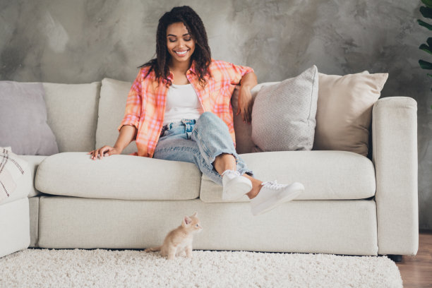 可爱漂亮的女士穿着橙色衬衫坐在沙发上玩小猫在室内房间的照片图片下载