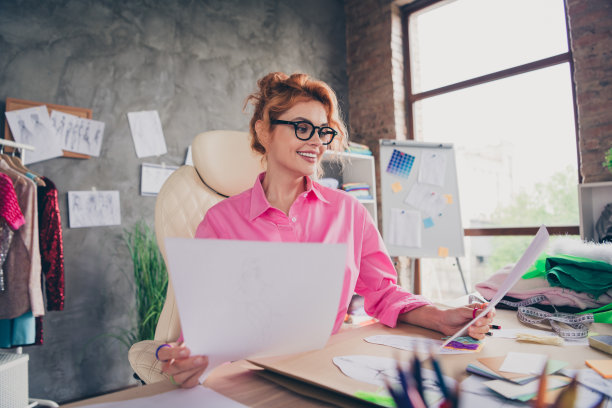 漂亮的年轻设计师的照片女裁缝坐椅子拿纸穿衬衫阁楼室内办公室室内图片下载