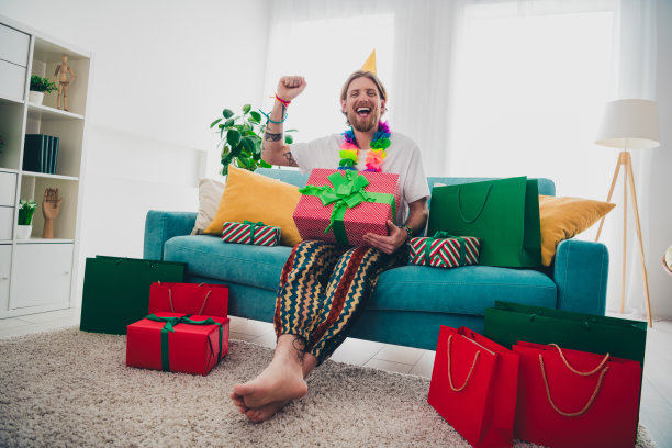 英俊的年轻人的全身照片坐在沙发赢得庆祝节日穿着睡衣度过休闲宽敞的房子室内房间图片下载