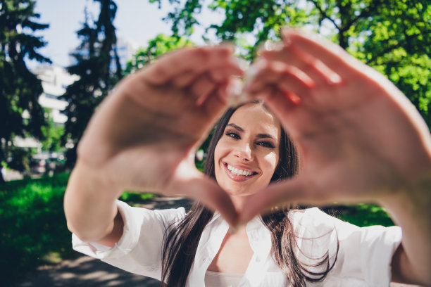 迷人的年轻开朗的女孩的照片显示心脏符号穿着白色的衣服在户外玩耍图片下载