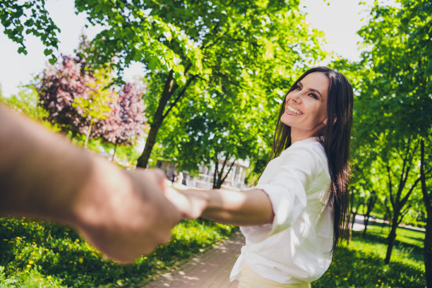 迷人的年轻开朗的女孩拉着伙伴手男友跟着穿着白色衣服在户外玩耍的照片图片下载