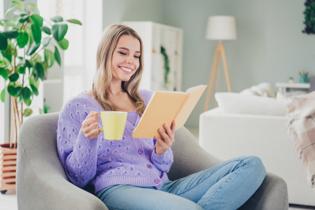 可爱开朗的女孩照片坐在扶手椅上喝茶看书穿着紫色的衣服在宽敞的屋子里消磨时光图片下载